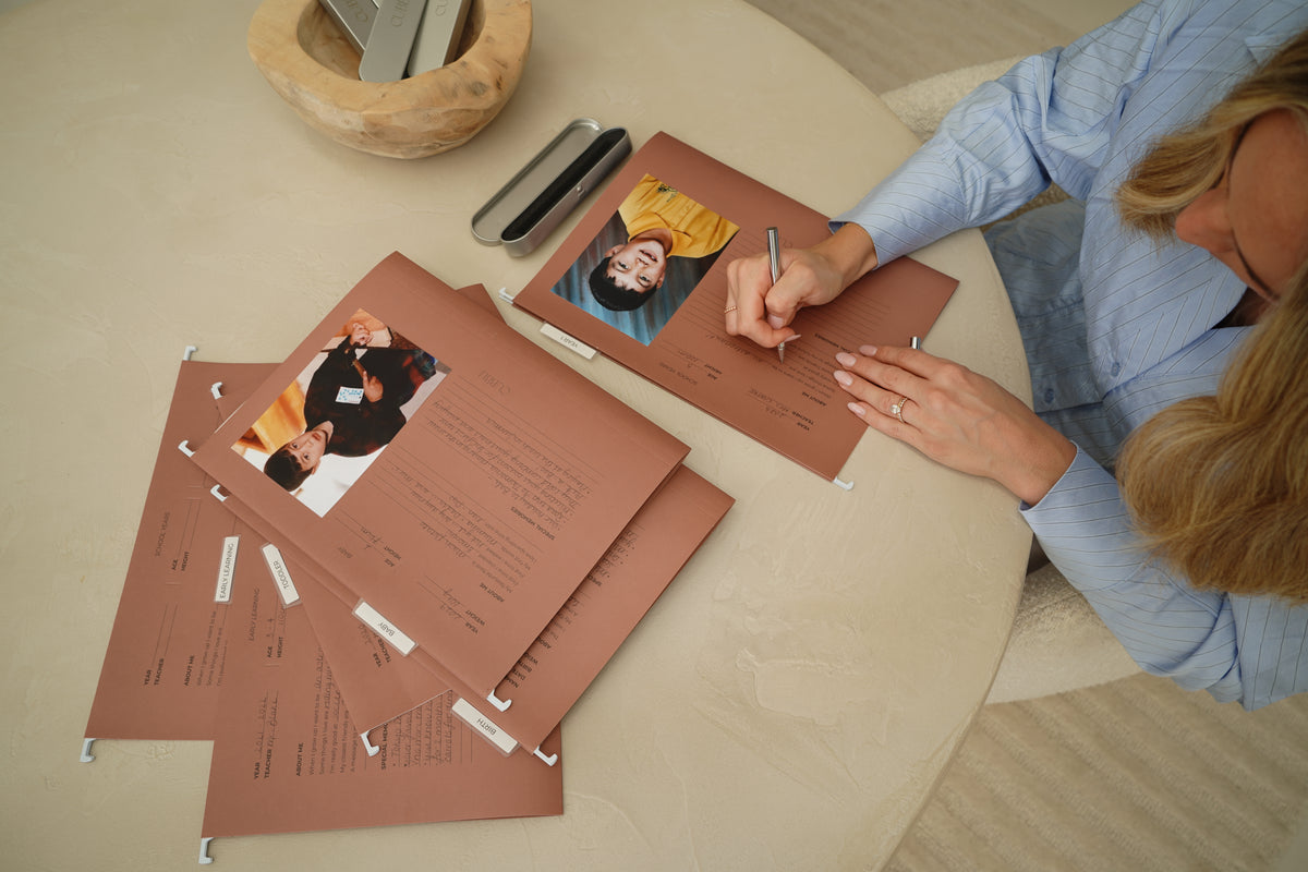 Overhead view of a woman filing children's artwork into CUBBLI keepsake folders